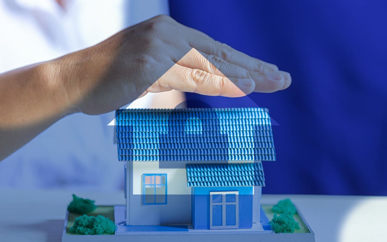 Una mano posada sobre una maqueta de una casa simulando la cobertura del seguro hogar